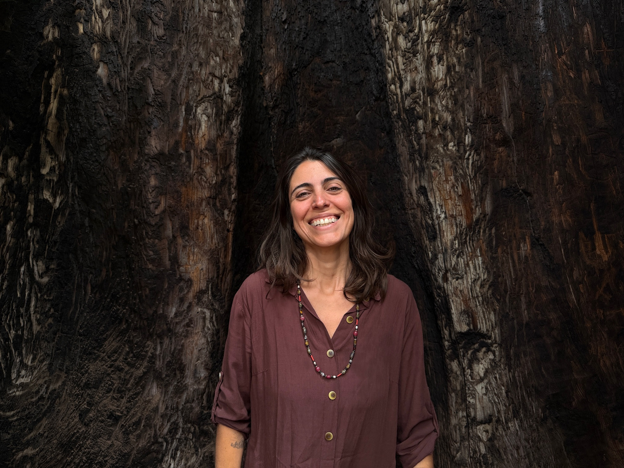 Marina sorrindo, de pé diante do tronco de uma sequoia gigante